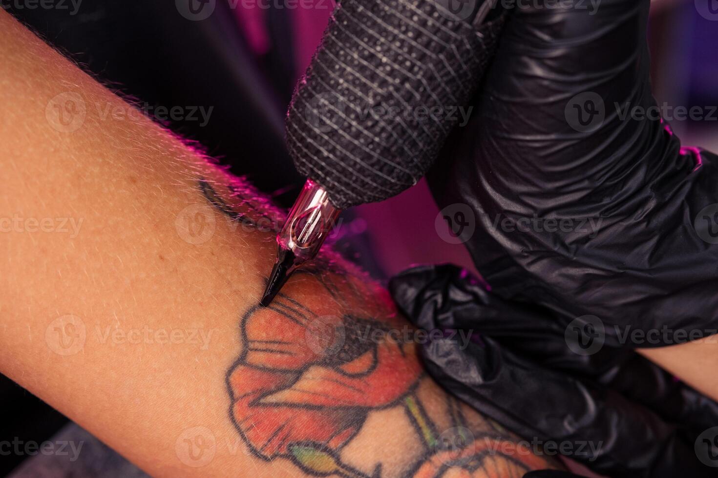 Tattoo machine in hands of professional master creating multicolored poppies photo