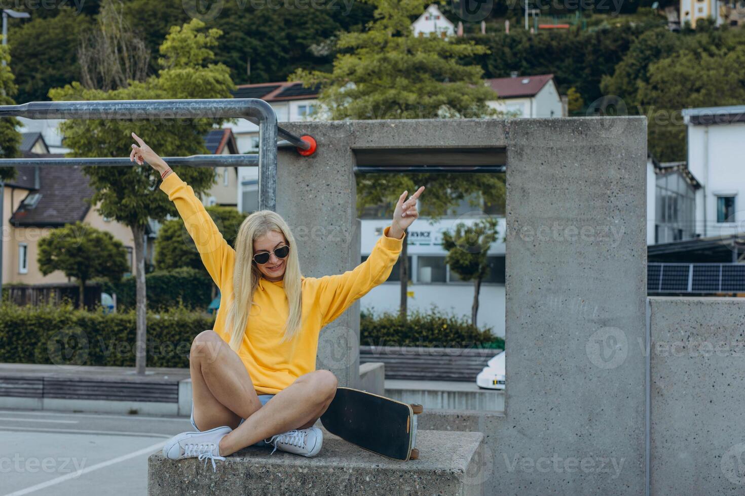 a young blonde girl in a yellow sweatshirt rides on the skateboard in the skate park photo