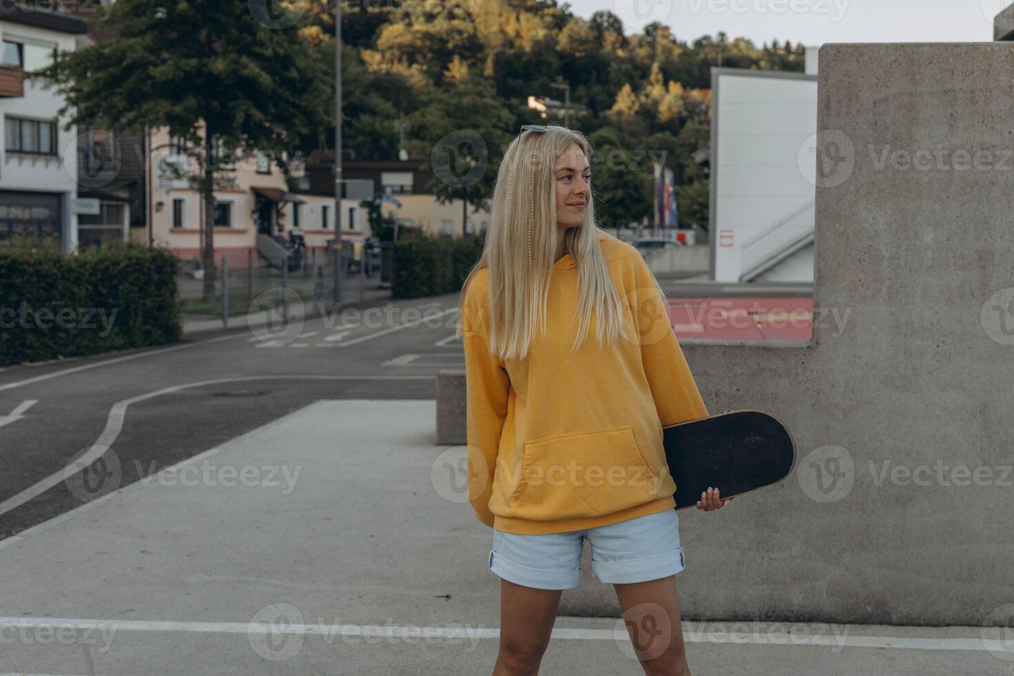 a young blonde girl in a yellow sweatshirt rides on the skateboard in the skate park photo