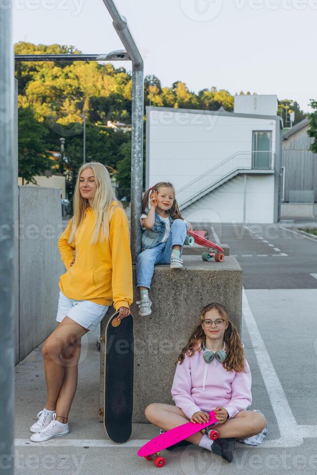 young mother with two daughters in a skate park Mother trains her daughter to skateboard. photo