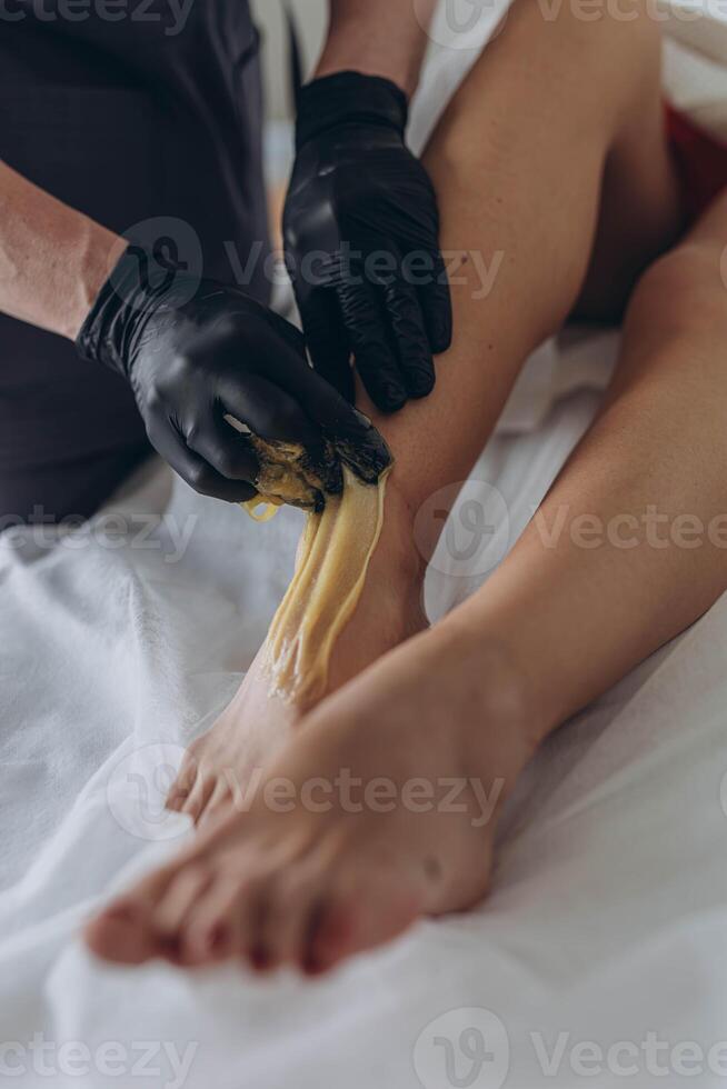 Beautician depilating young woman's legs with liquid sugar in spa center photo