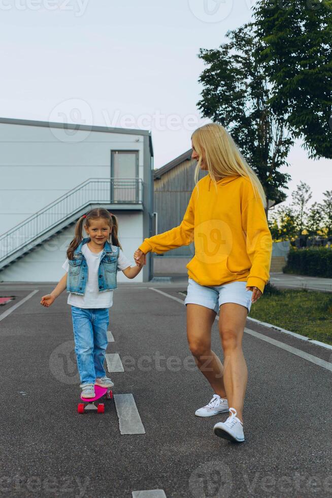 Active little girl and mom enjoy skateboarding. Mother trains her daughter to skateboard. photo