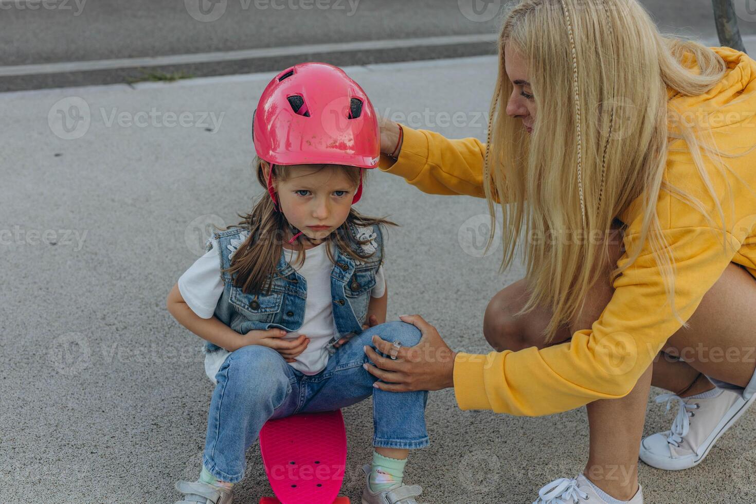 Mom helping her daughter to put on a helmet and ride a skateboard photo