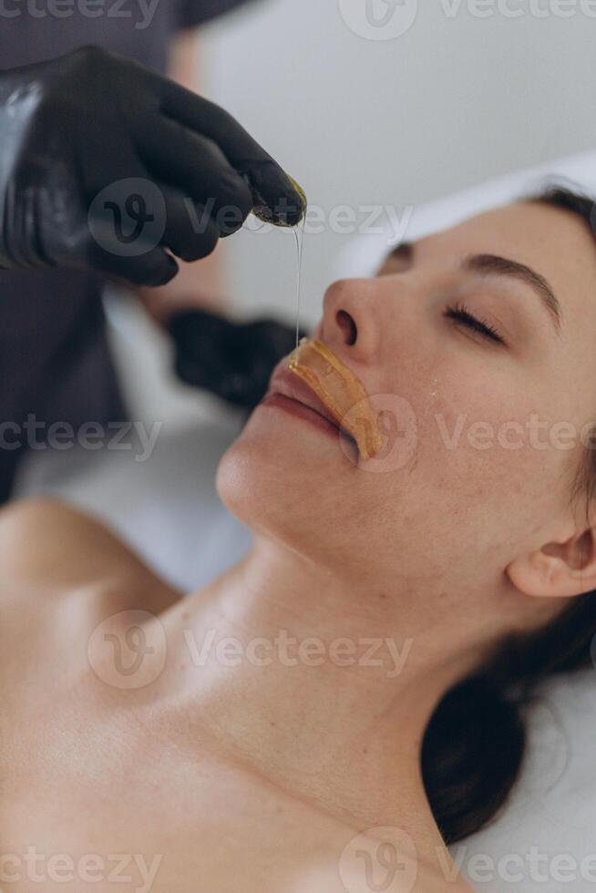 Removing hair above upper lip of young woman in salon. shugaring depilation. photo