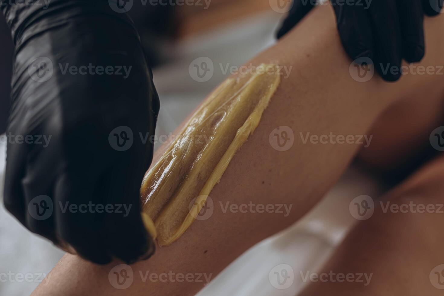 Beautician depilating young woman's legs with liquid sugar in spa center photo