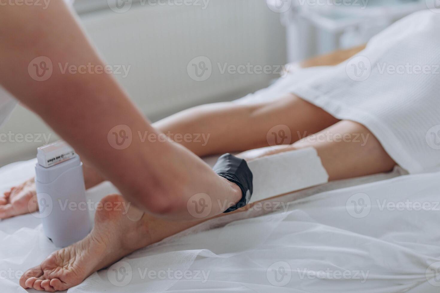 Beautician depilating young woman's legs with liquid sugar in spa center photo