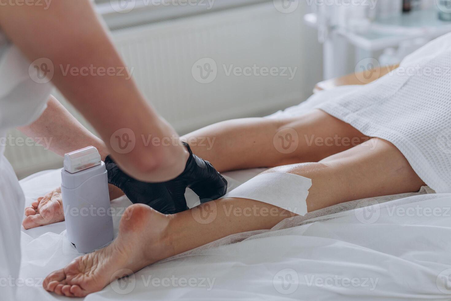 Beautician depilating young woman's legs with liquid sugar in spa center photo