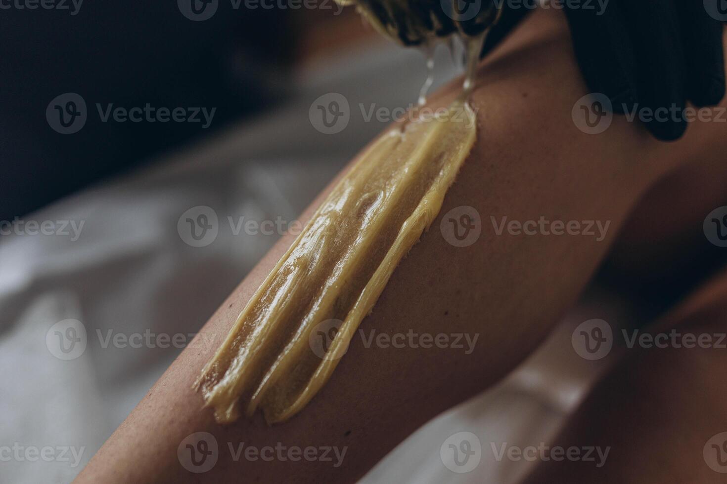Beautician depilating young woman's legs with liquid sugar in spa center photo