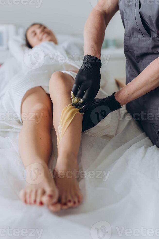 Beautician depilating young woman's legs with liquid sugar in spa center photo