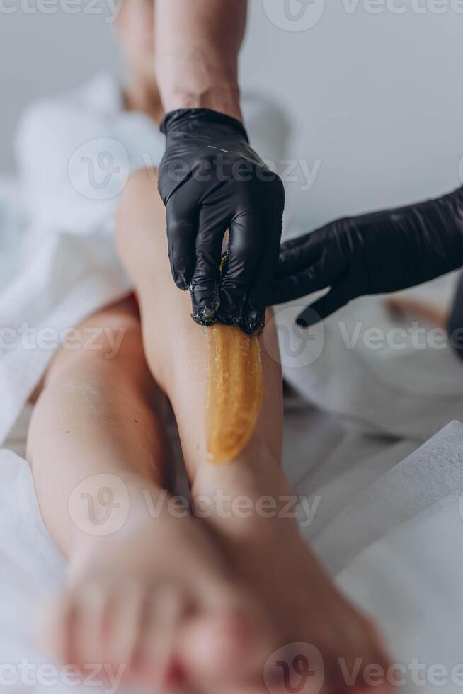 Beautician depilating young woman's legs with liquid sugar in spa center photo