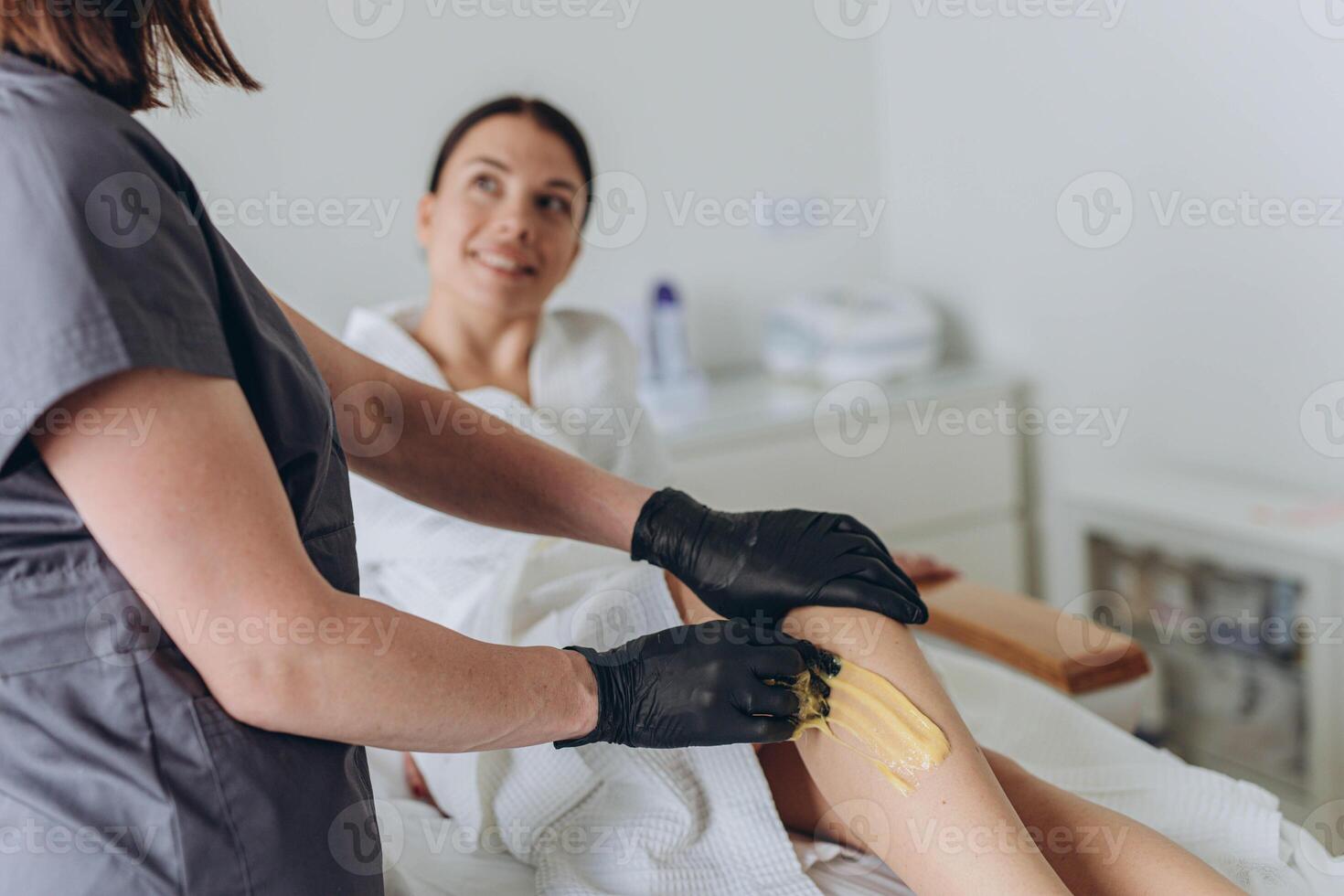 Beautician depilating young woman's legs with liquid sugar in spa center photo