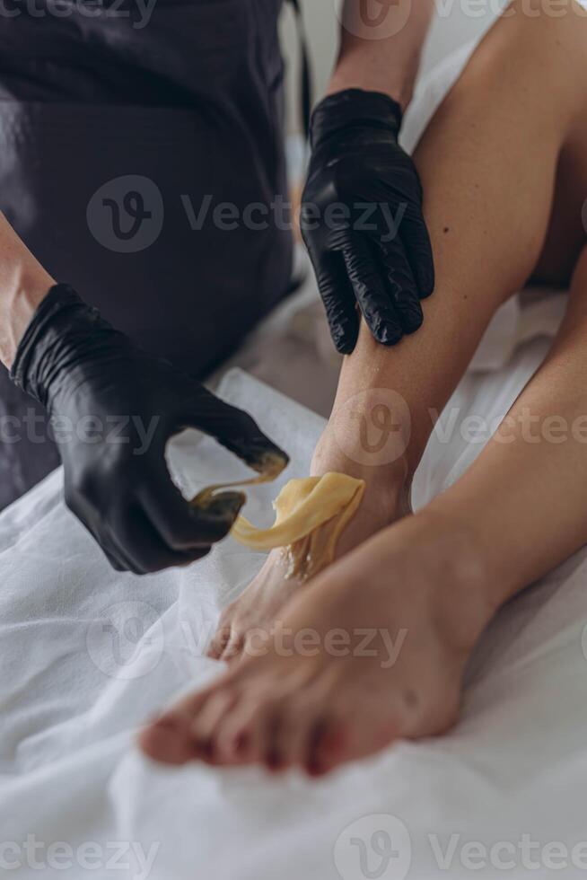 Beautician depilating young woman's legs with liquid sugar in spa center photo