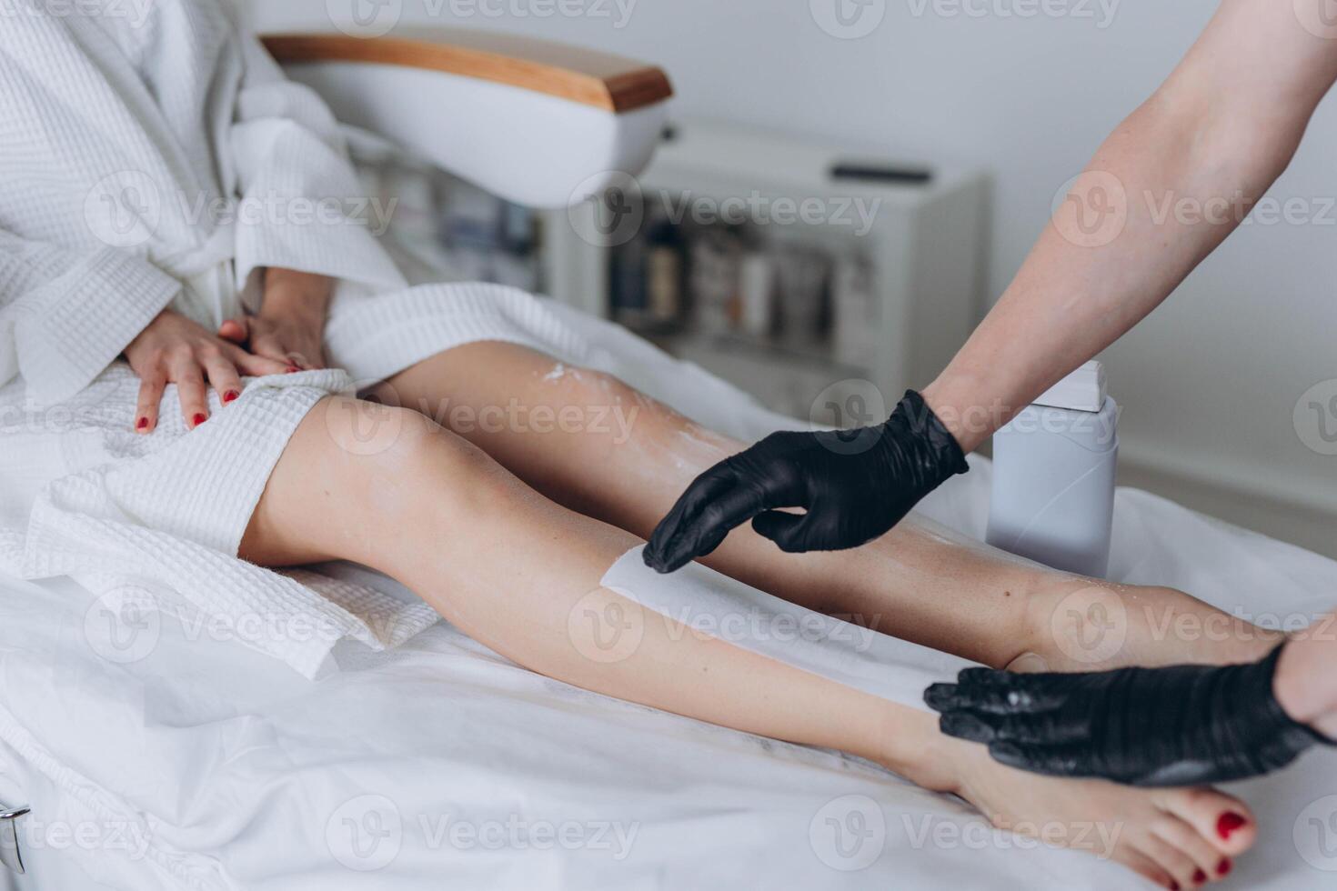 Beautician depilating young woman's legs with liquid sugar in spa center photo