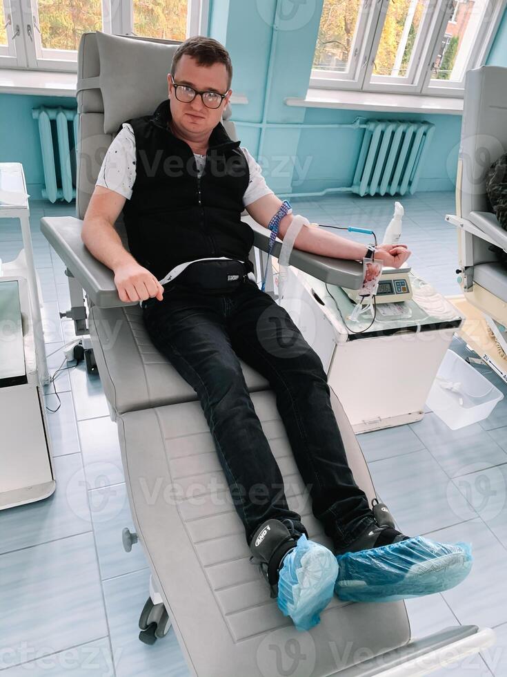 Young man making blood donation in hospital, focus on hand. Male donor gives blood in a mobile blood donation center photo