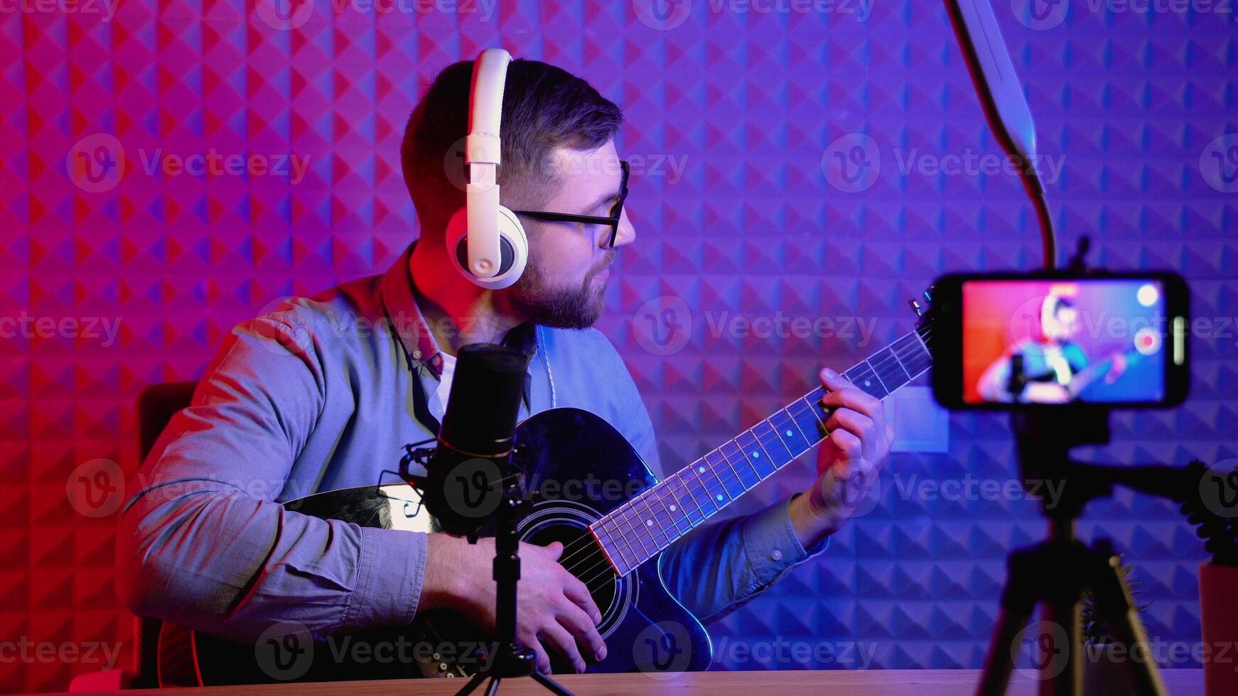 Young influencer playing guitar during podcast or live streaming for audience from mobile phone at home - concept of art, hobby and blog photo