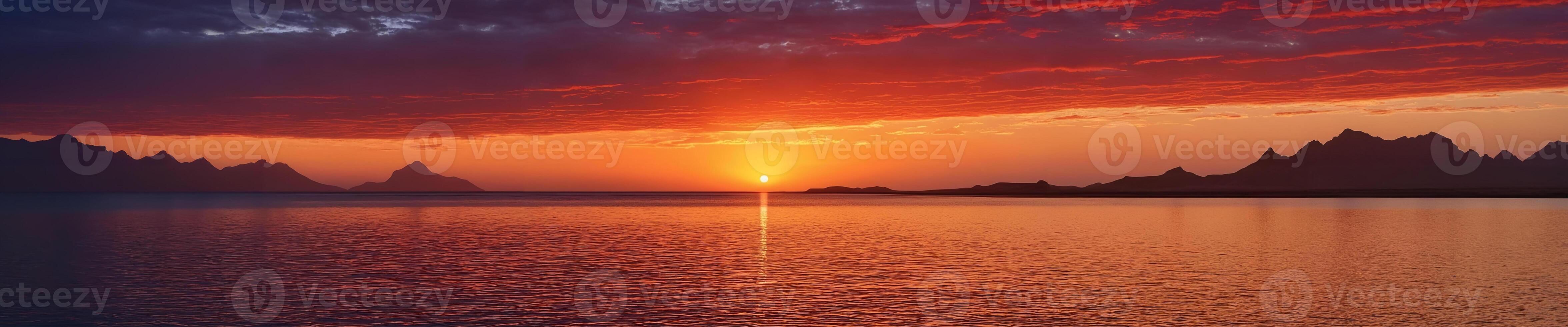 A beautiful sunset over a large body of water, with mountains in the background. The sun is setting, casting a warm glow on the scene, and creating a serene atmosphere. photo