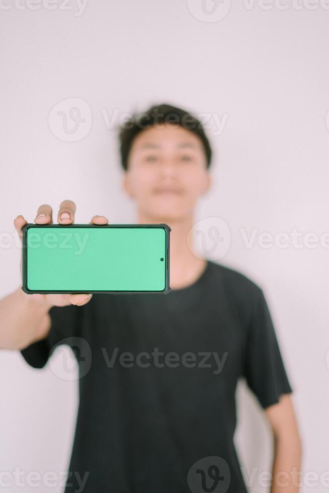 A Southeast Asian man holding a greenscreen phone, ready for customization. Perfect for adding your own content or app interface in a marketing or promotional context photo