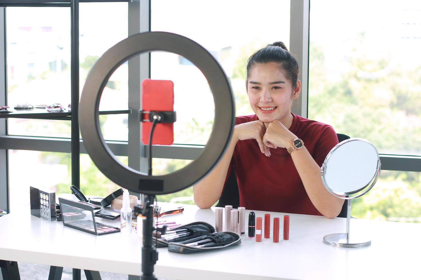 Beautiful Asian woman blogger recording on red smartphone for make up tutorial in Cosmetics Vlog website. Youtber and Marketing in social media concept. photo