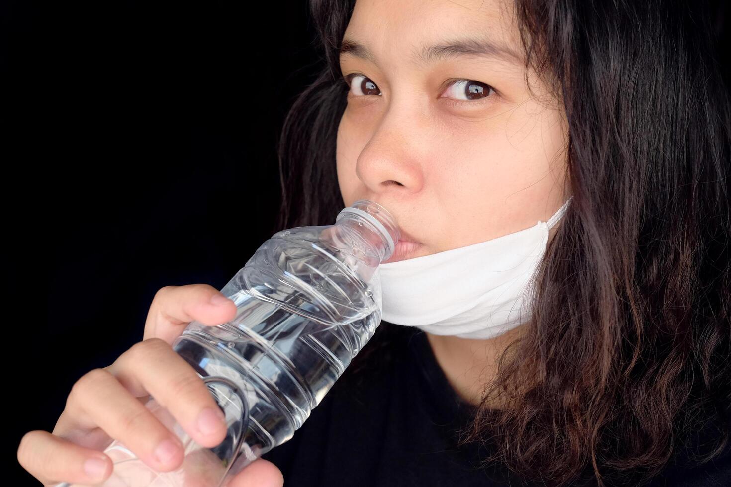 Asian Thai woman wearing a white cloth mask for prevent the Covid-19 or Corona virus and Air Pollution Value Pm 2.5 in Thailand and drinking a bottled mineral water. Health and illnes concept photo