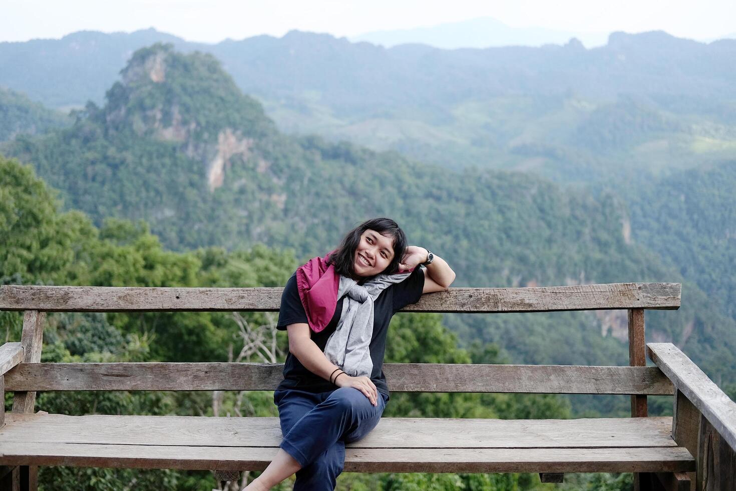 Asian woman sitting and relaxing on wooden bench on terrace for freedom journey with valley mountain and foggy in natural and travel destination in tropical rain forest photo