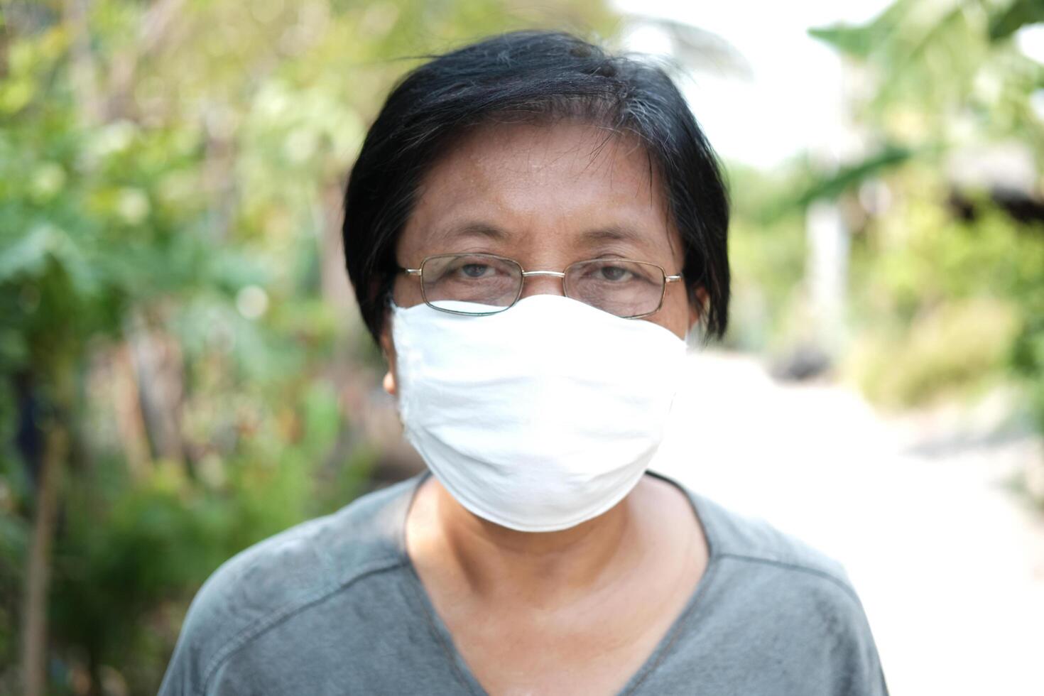 Asian old woman wearing glasses and white cloth mask for prevent the Covid-19 or Corona virus in Thailand and protect for Air Pollution Value Pm 2.5. Health and medicine of elderly in garden concept photo