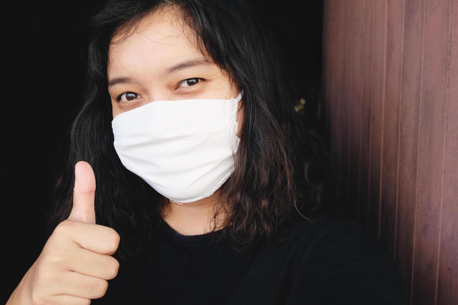 Asian Thai woman wearing a white cloth mask for prevent the Covid-19 or Corona virus in Thailand and Thumbs up and smiling for protection in Air Pollution Value Pm 2.5. Health and medical concept photo