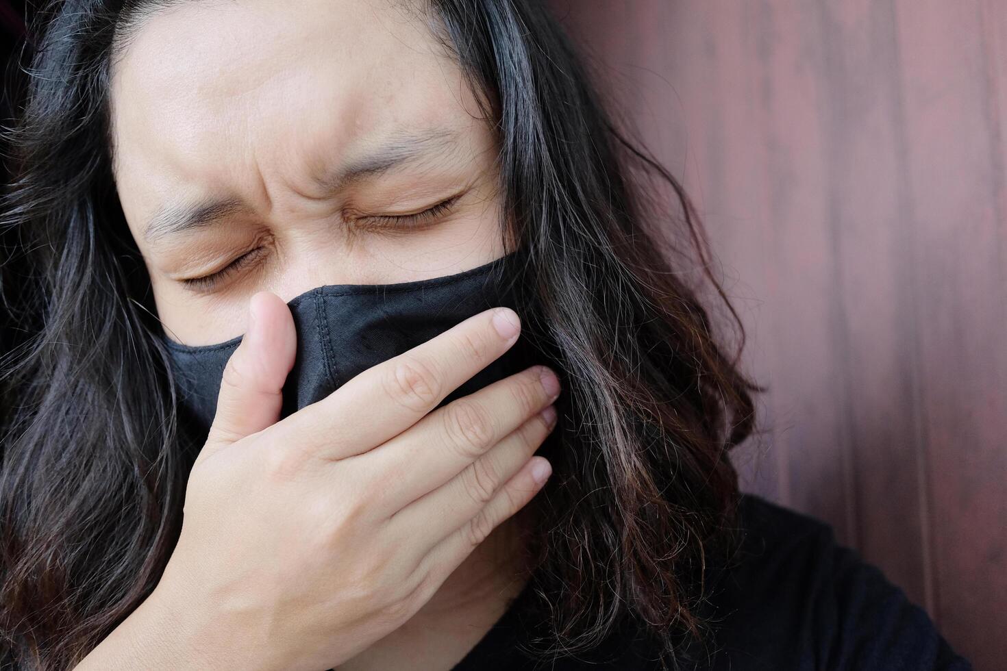 Asian Thai woman wearing a black cloth mask for prevent the Covid-19 or Corona virus and Epidemic disease at Thailand and around the world. She is coughing and headache. Health and illness concept photo