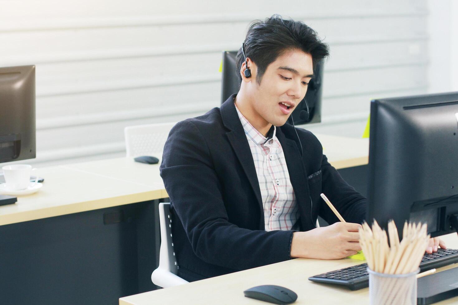 Businessman Call Center and technical Support staff with headset talking and writing in yellow paper note for job. Asian customer support team. photo