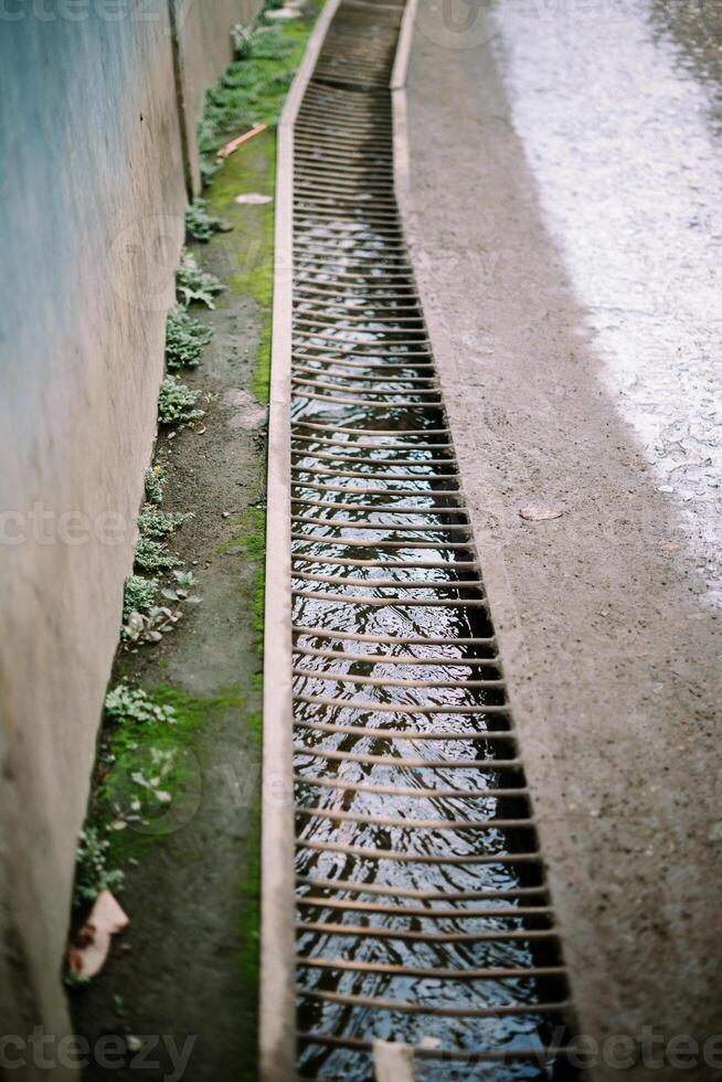 A stream of household runoff flows beneath, shielded by sturdy iron supports to prevent accidental slips, blending utility with safety photo