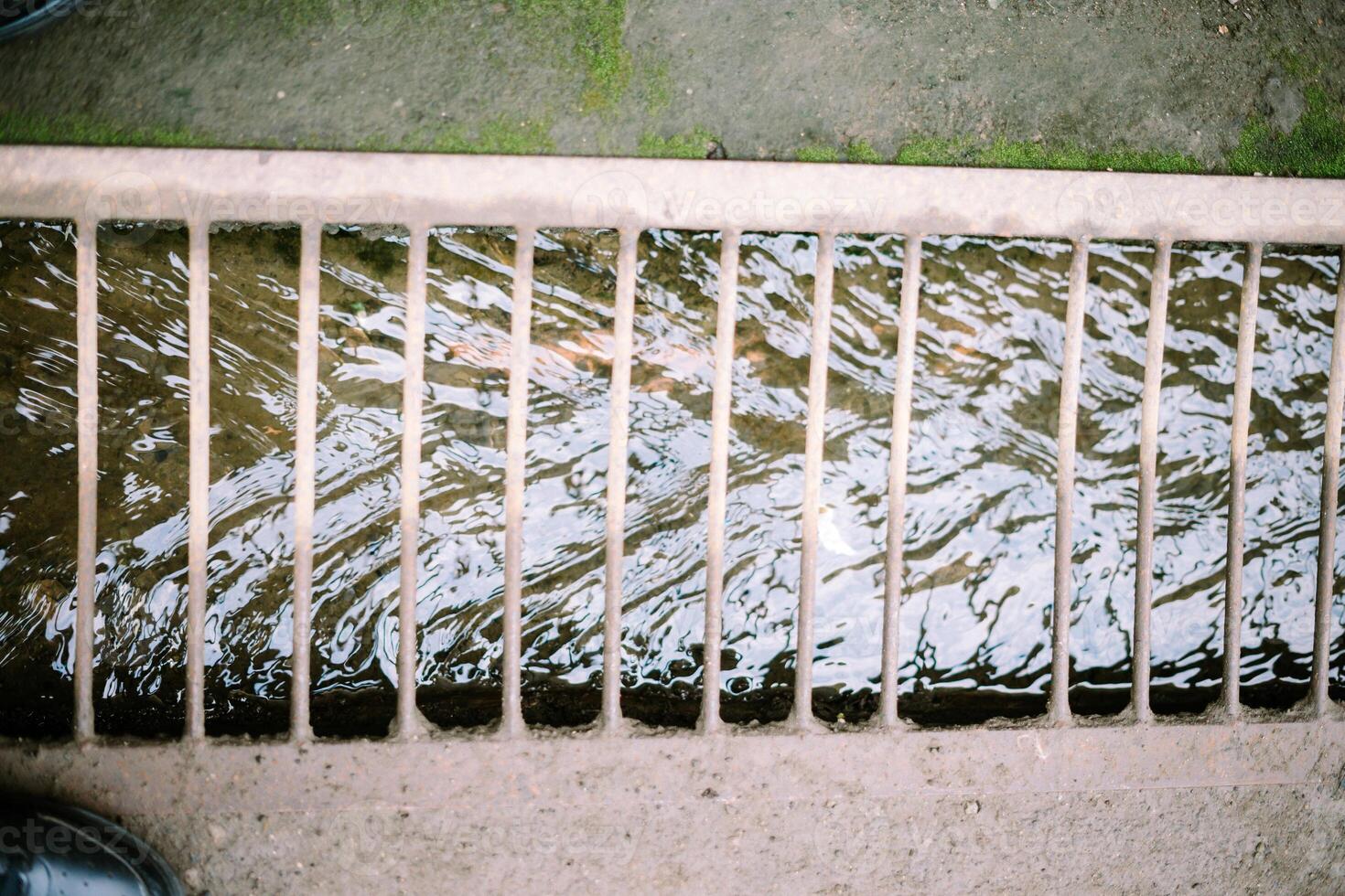 A stream of household runoff flows beneath, shielded by sturdy iron supports to prevent accidental slips, blending utility with safety photo
