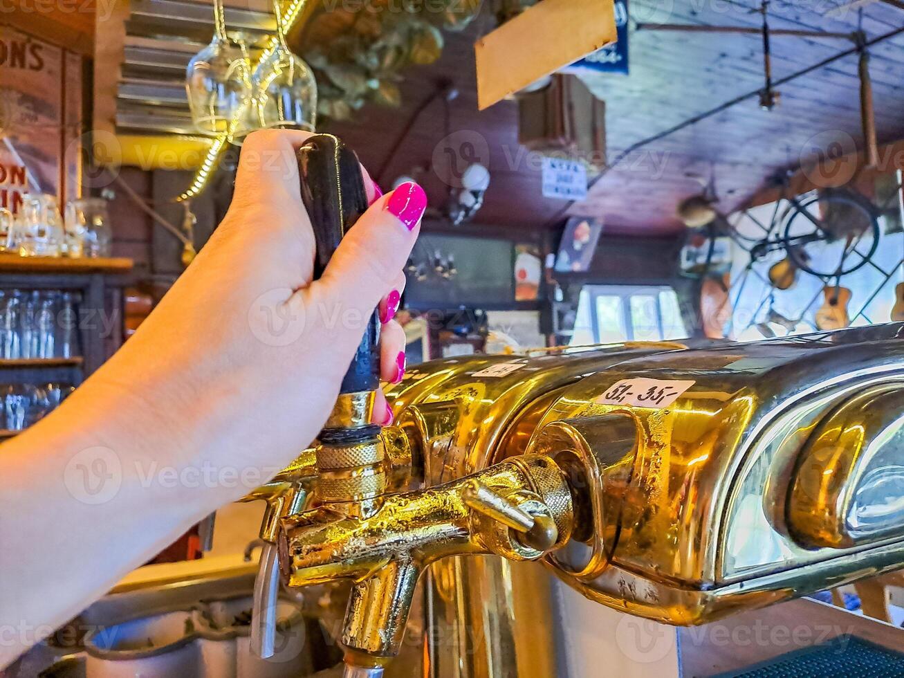 bartender hand at beer tap pouring a draught beer in glass serving in a bar photo