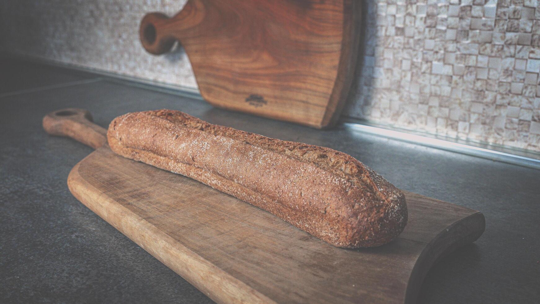 Baguette of dark buckwheat bread on a walnut wooden cutting board photo