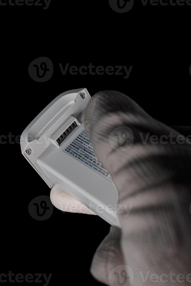 Gloved Hand Holding Drone Battery Against Black Background at Night photo