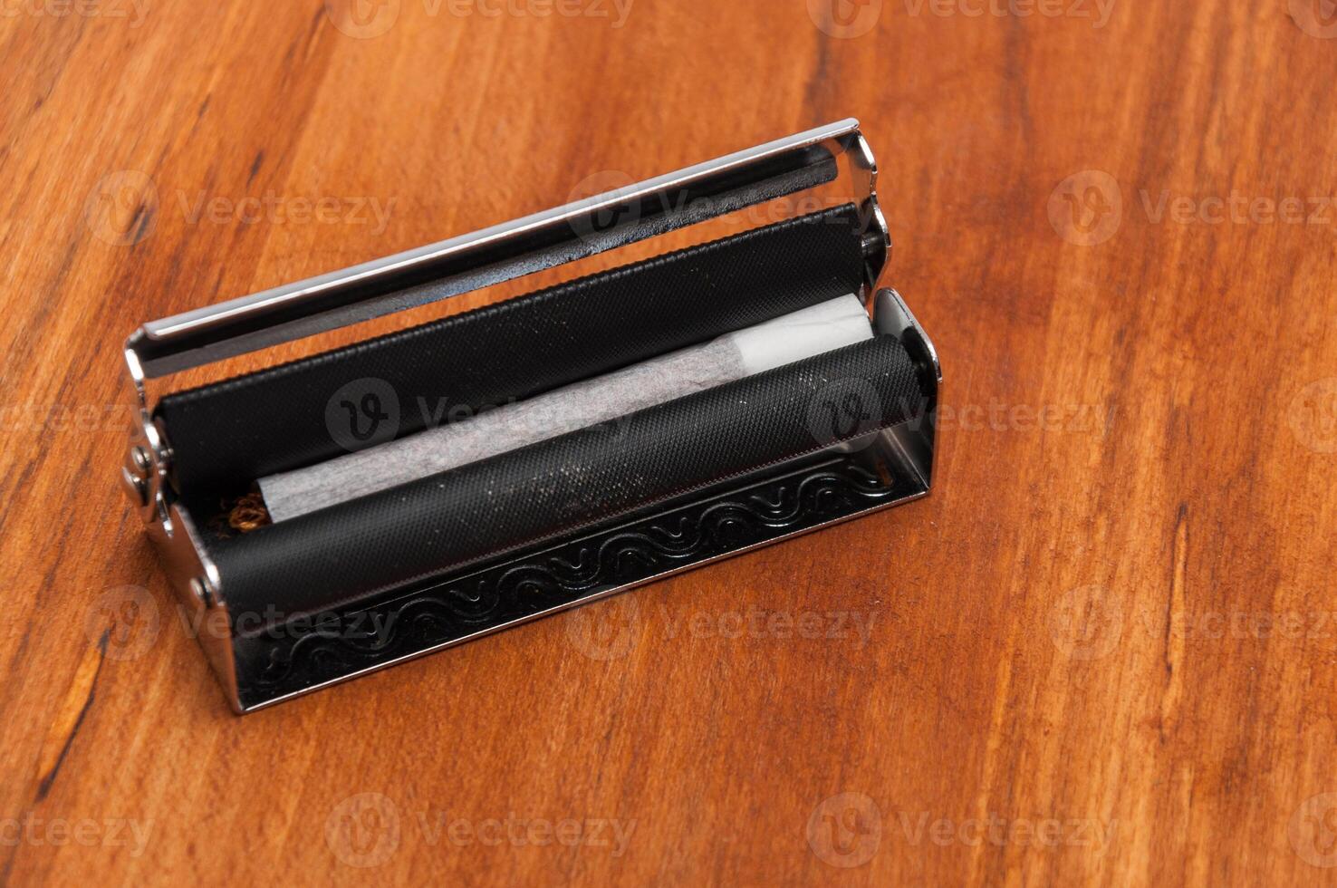 Hand rolled cigarette in the machine on the wooden background photo