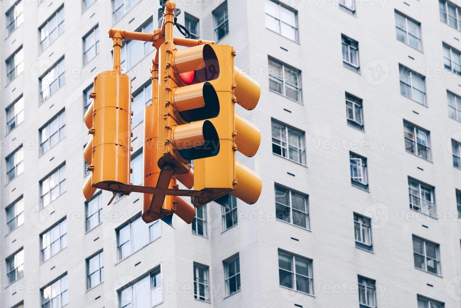 Yellow traffic light showing red light with a grey building on the background photo