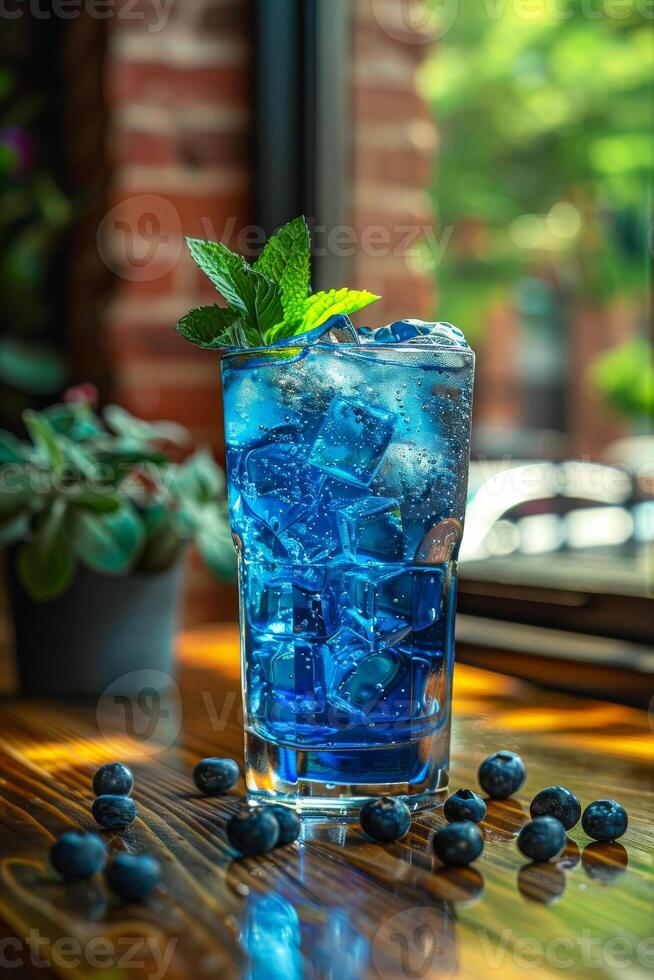 A tall glass of blue liquid with a sprig of mint on top photo