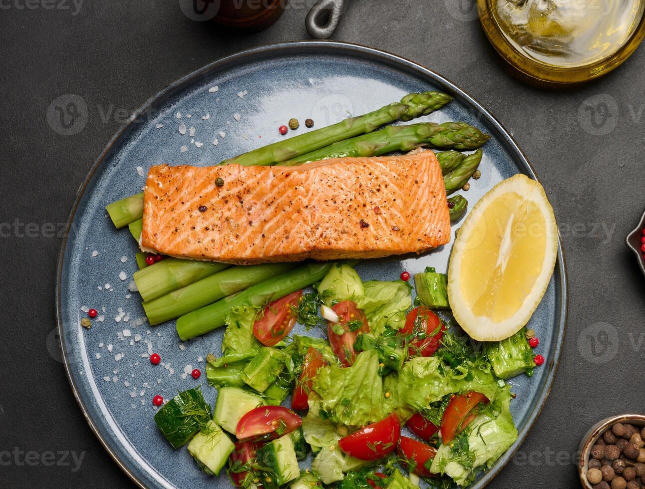 Healthy lunch with grilled salmon with asparagus and fresh tomato and cucumber salad, a row of lemon slice. photo