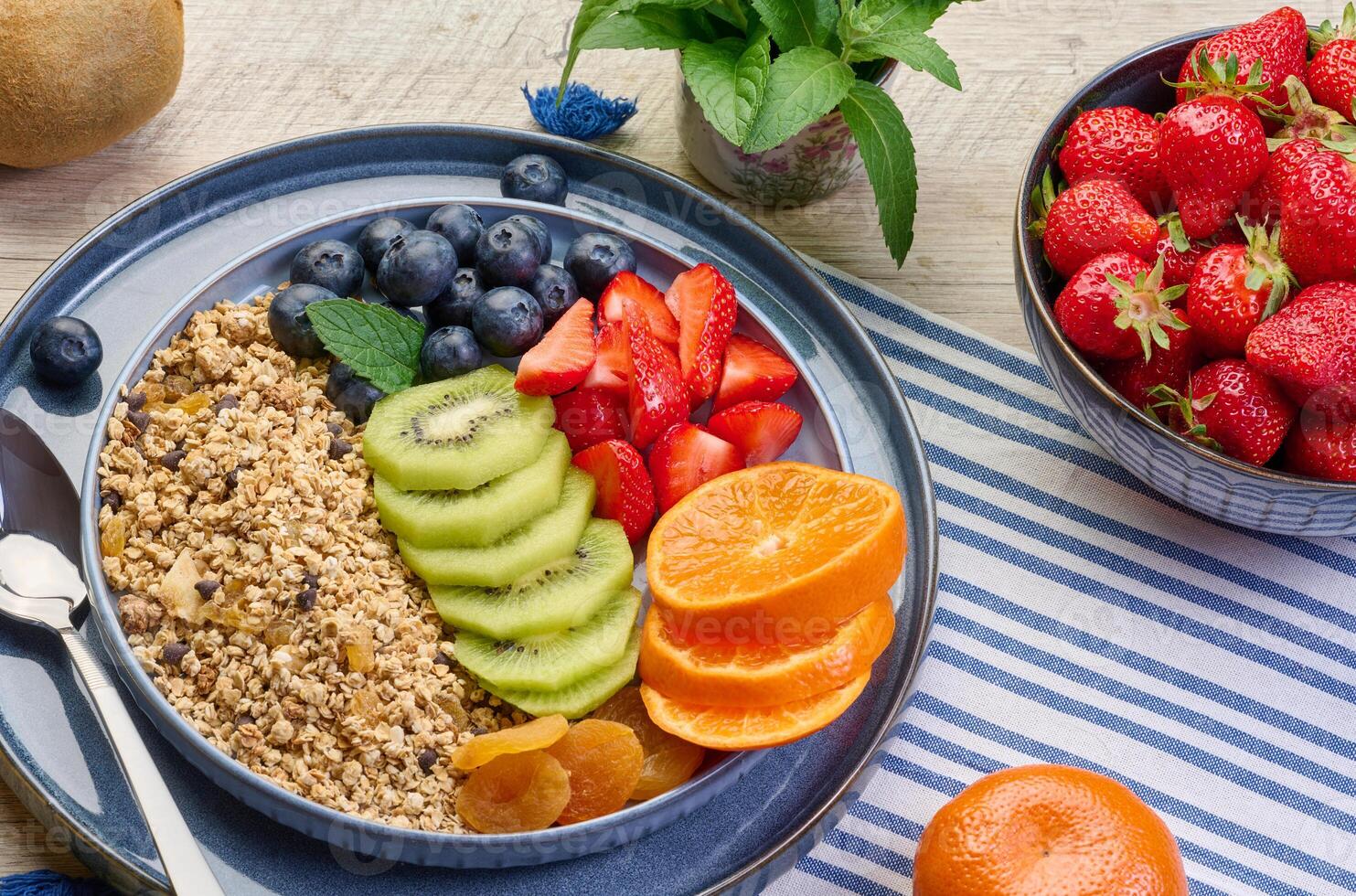 Granola with strawberries, kiwi, banana and blueberries in a round plate on a white table. photo