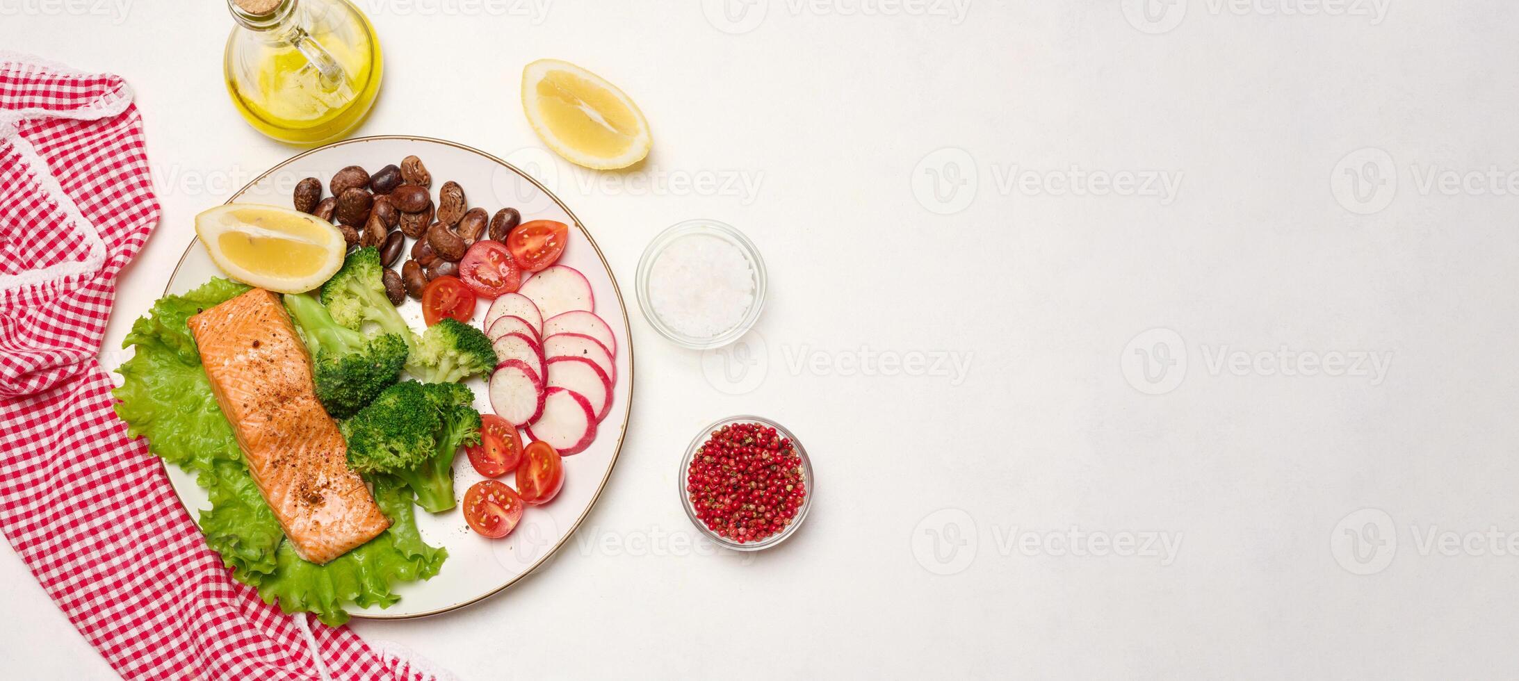 Healthy lunch with grilled salmon on green lettuce, next to vegetables, tomatoes, radishes, broccoli and a portion of beans. photo