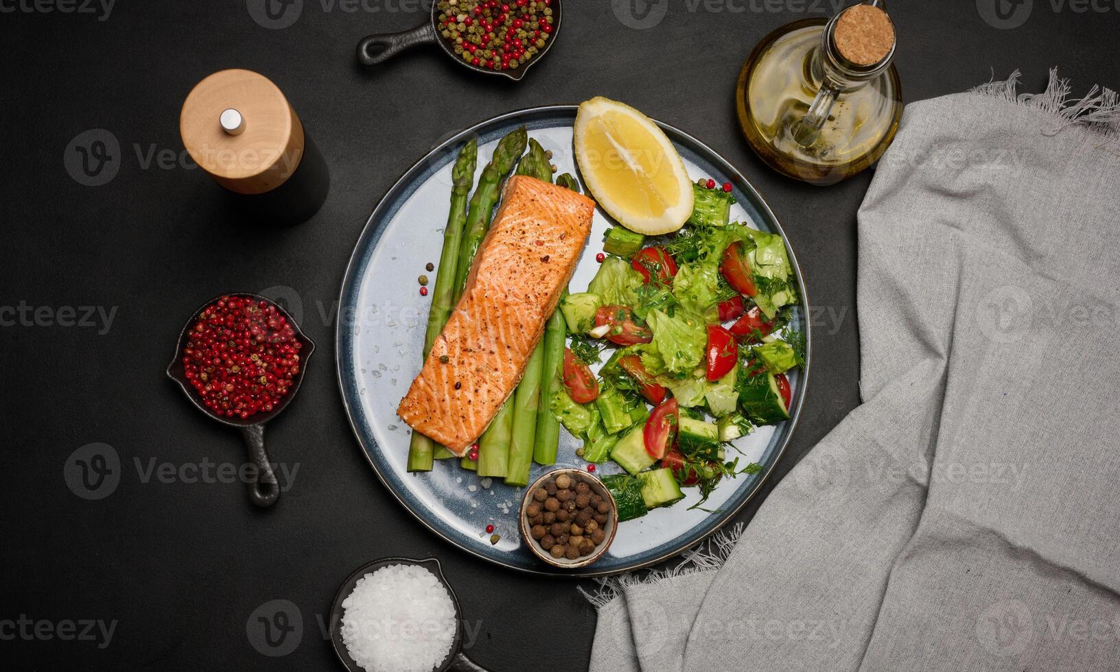 Healthy lunch with grilled trout with asparagus and fresh tomato and cucumber salad, a row of lemon slice. photo