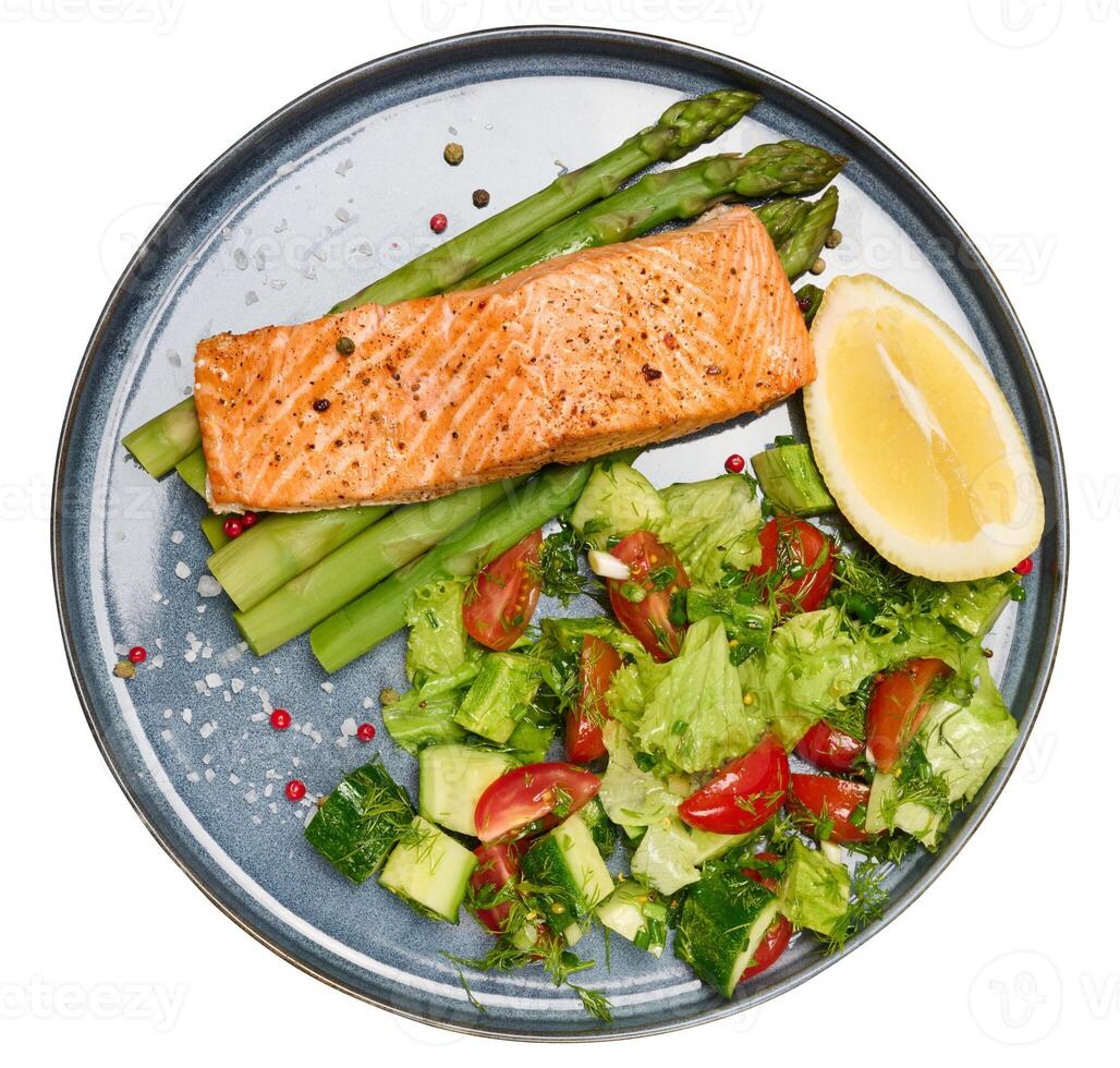 Healthy lunch with grilled trout with asparagus and fresh tomato and cucumber salad, a row of lemon slice. photo