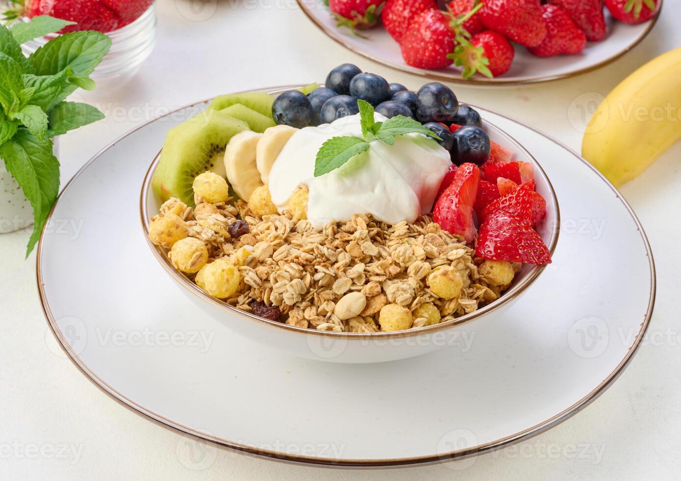 Granola with strawberries, kiwi, banana and blueberries in a round plate topped with yogurt on the table. photo