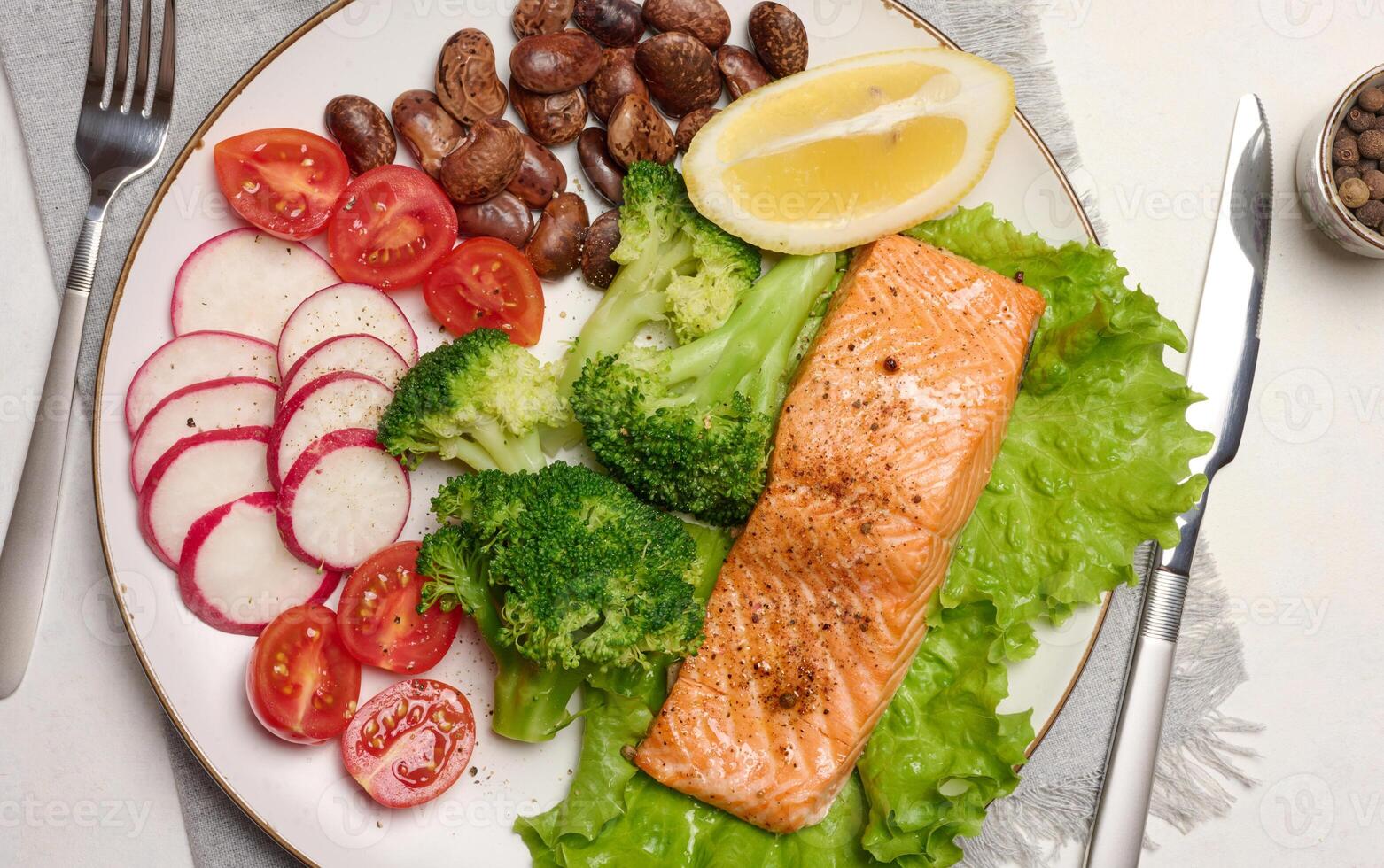 Healthy lunch with grilled salmon on green lettuce, next to vegetables, tomatoes, radishes, broccoli and a portion of beans. photo
