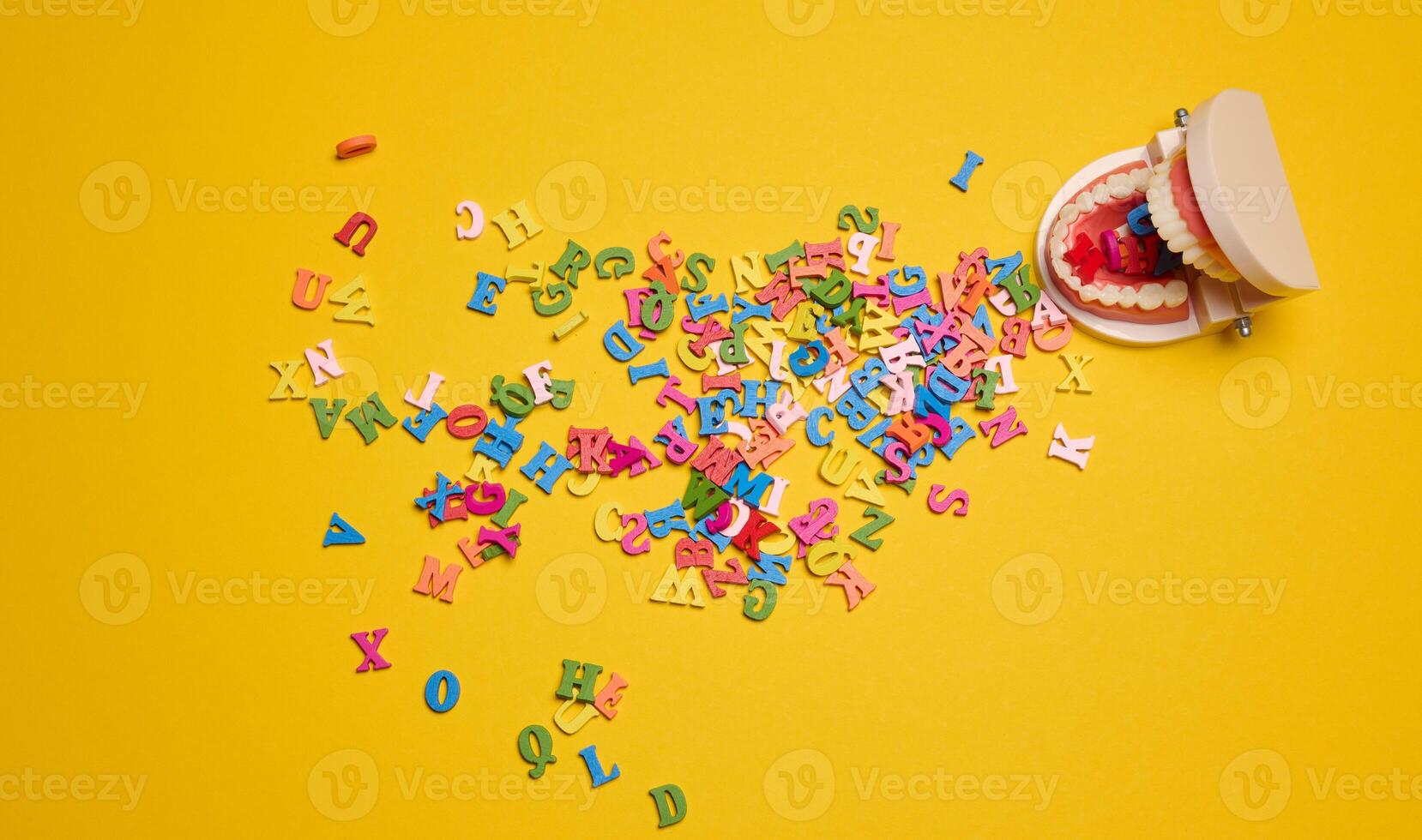 Artificial jaw with teeth, from which multi-colored letters of the alphabet spilled out on a yellow background photo