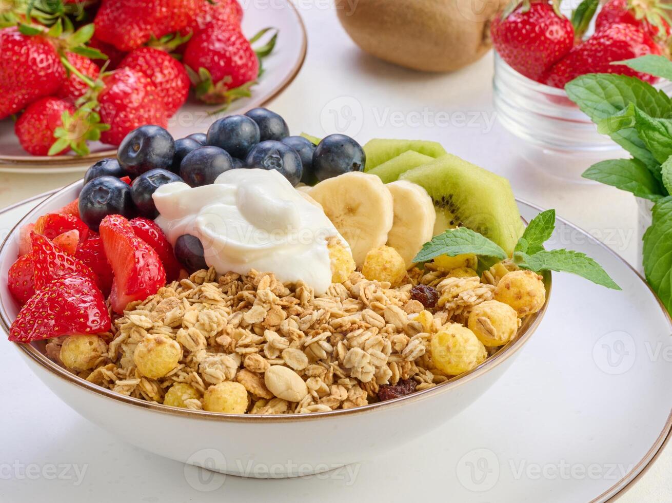 Granola with strawberries, kiwi, banana and blueberries in a round plate topped with yogurt on the table. Healthy and tasty food photo