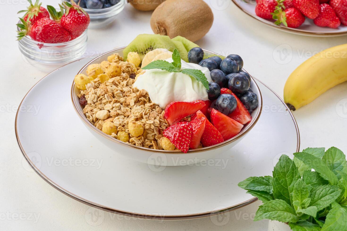 Granola with strawberries, kiwi, banana and blueberries in a round plate on a white table. photo
