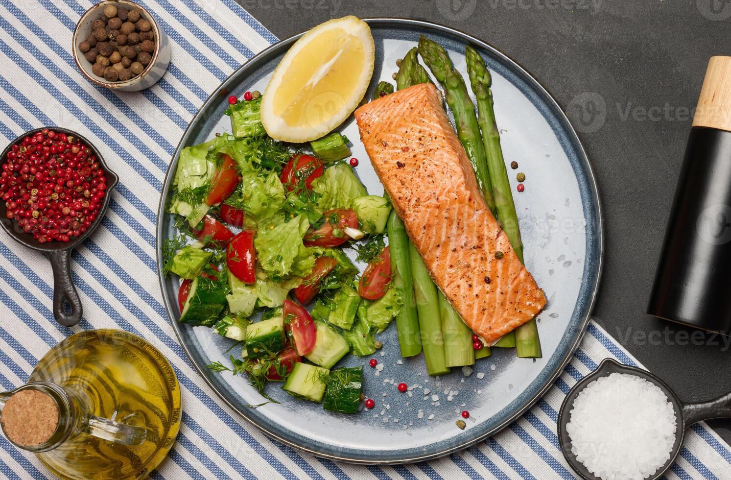 Healthy lunch with grilled salmon with asparagus and fresh tomato and cucumber salad, a row of lemon slice. photo