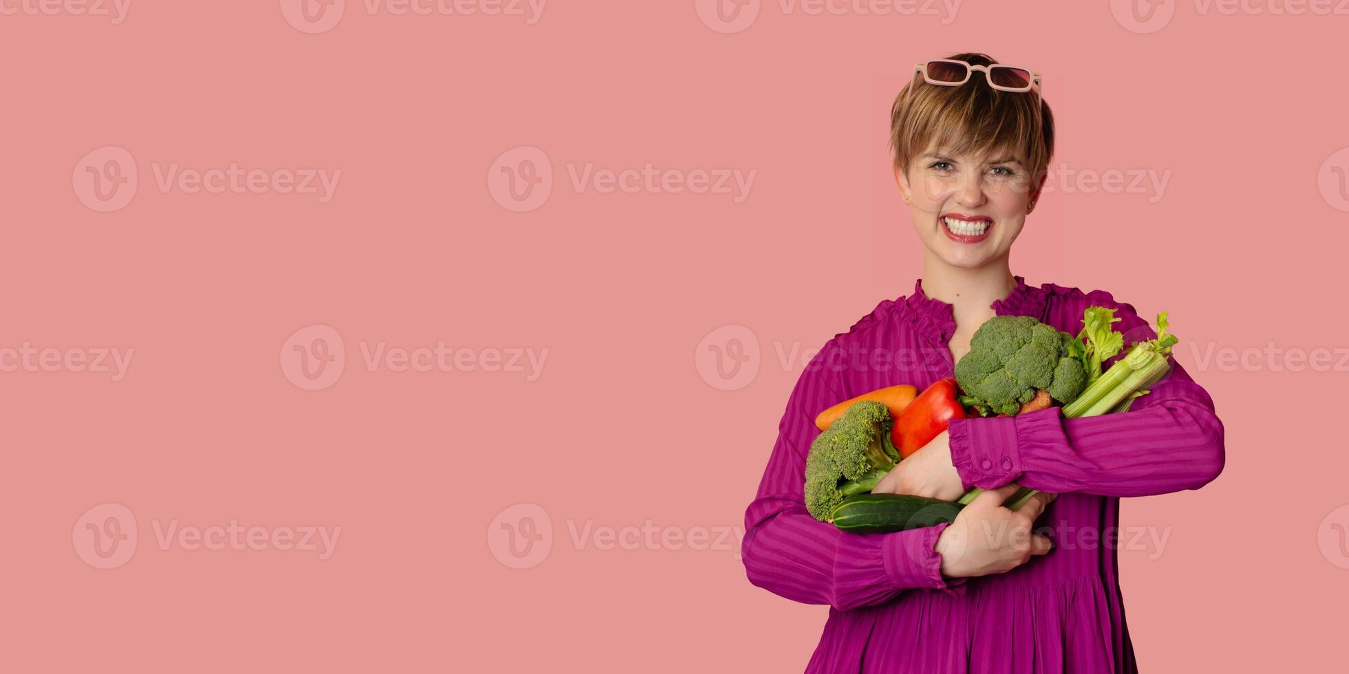 A studio shot of a young woman holding a lot of fresh vegetables in her hands. The concept of healthy eating. Vegetarianism. A panoramic banner with a copy of the space. photo