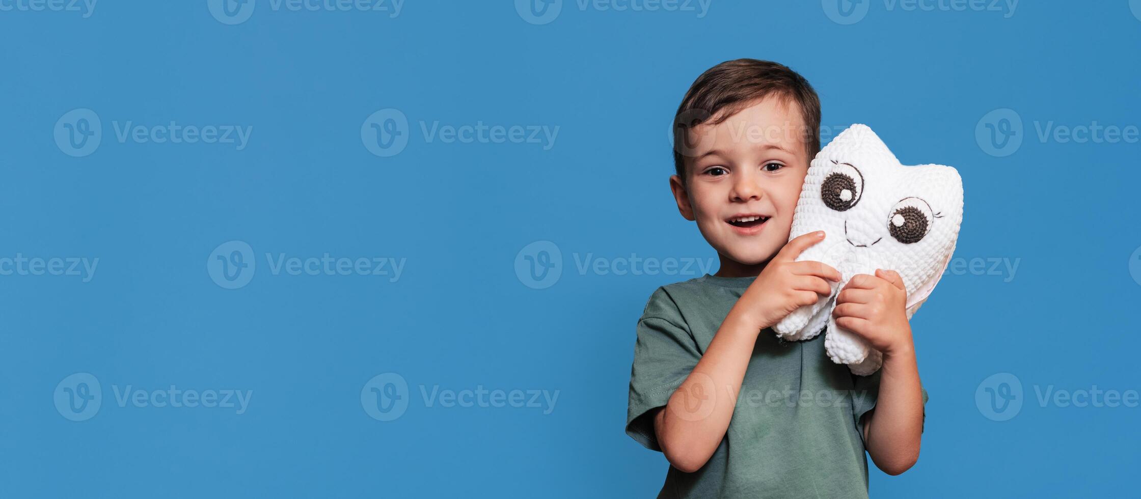 A smiling boy with healthy teeth holds a toothbrush and a plush tooth on a blue background. Pediatric dentistry. A place for your text. Panoramic photo. photo