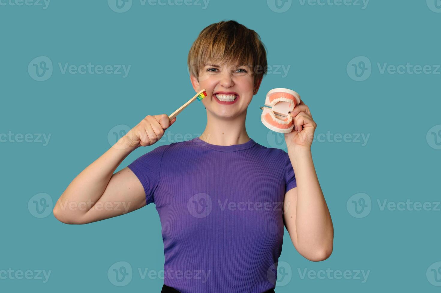A close-up of a young woman with a model of a denture in her palm and a toothbrush in her hand on a blue background The concept of oral care. photo